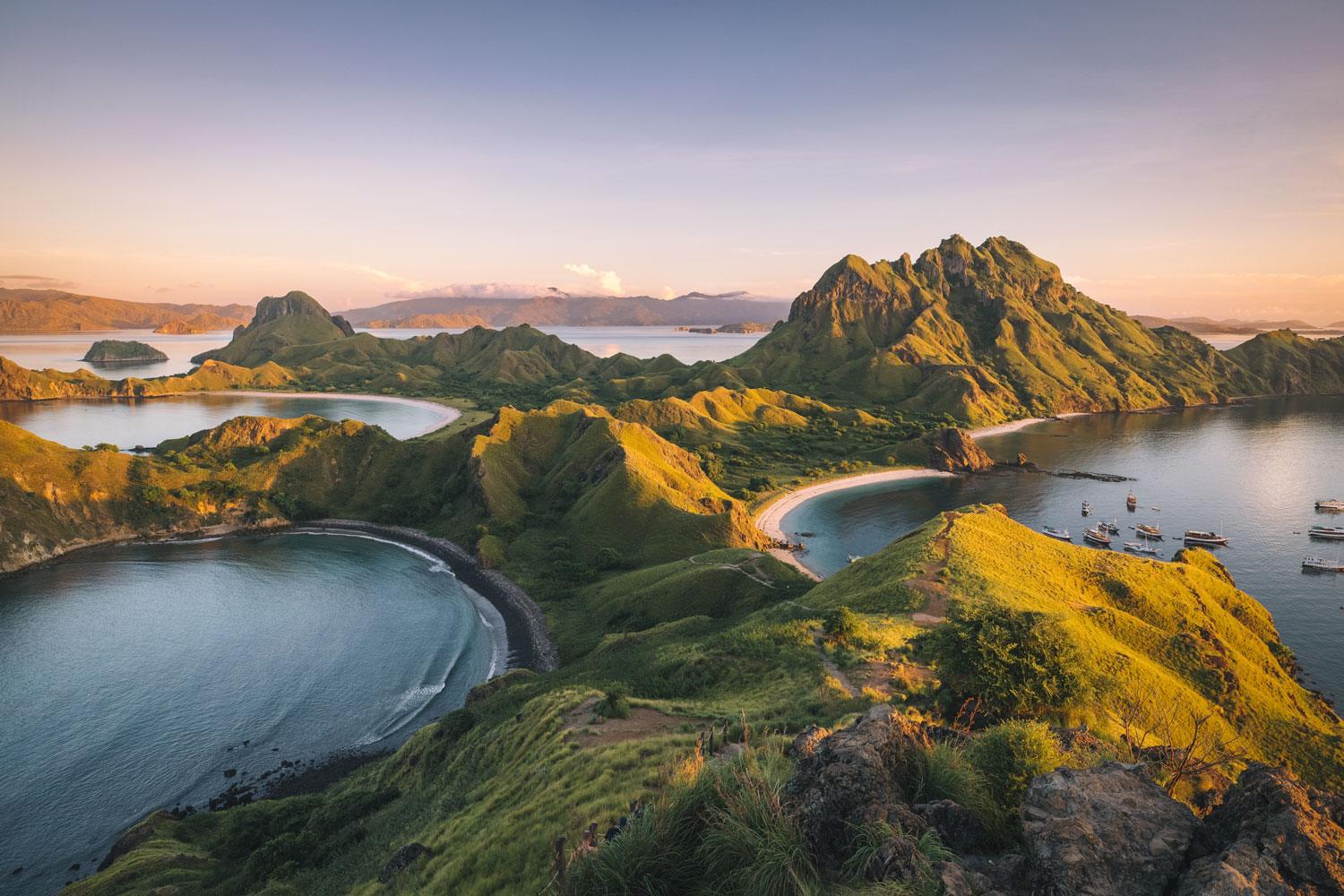 Terms and conditions. Lush green hills surround tranquil bays and islands, with boats moored in calm waters under a vibrant, sunset sky.
