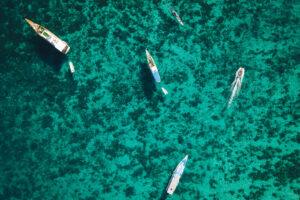 Aerial view of several boats gliding over crystal-clear turquoise waters with visible coral reefs below.