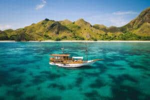 A wooden boat anchored in clear turquoise waters near a lush, green mountainous shoreline.