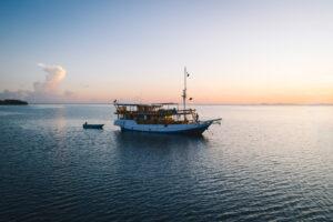 A wooden boat anchored in calm waters at sunset, reflecting hues of orange and pink in the sky.