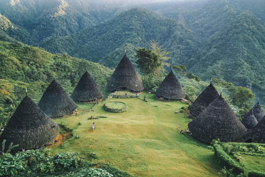 WaeRebo village. Aerial view of traditional cone-shaped huts surrounded by lush green mountains and landscaped gardens.