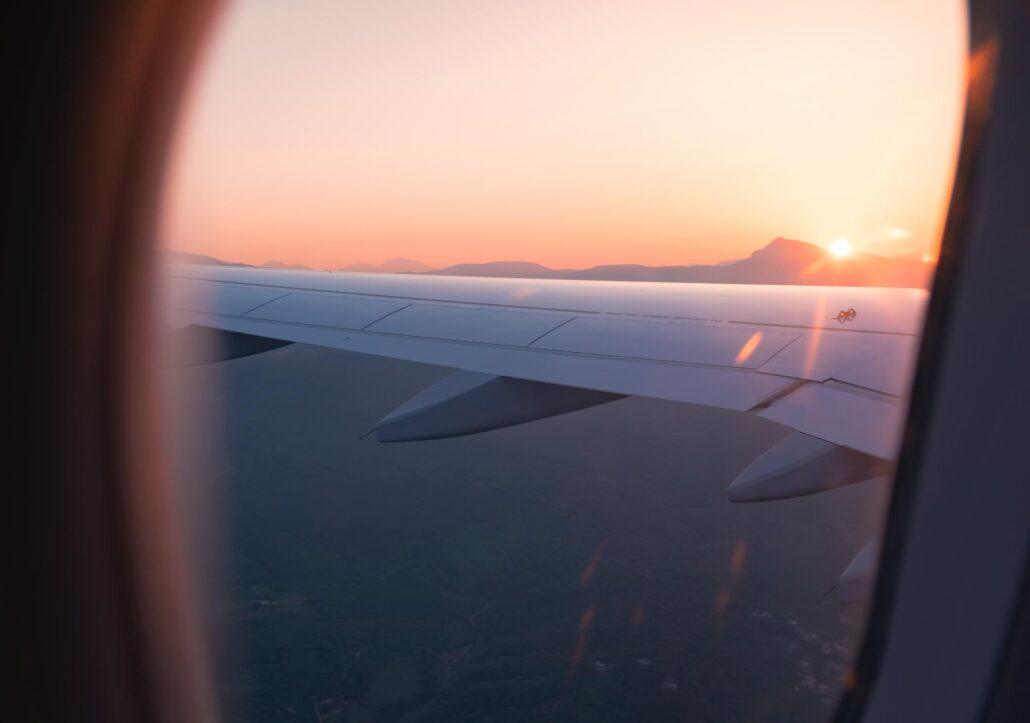 View from an airplane window showcasing a wing against a sunset with mountains in the distance.