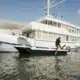 3 days shared trip. A diver boards a small boat next to a large white yacht on calm water under a blue sky with scattered clouds.