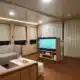 3 days shared trip. Modern living room featuring a gray sofa, large TV, wooden decor, and curtains, illuminated by warm lighting.