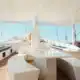 3 days shared trip. Interior view of a modern boat featuring a curved white seating area, a central table, and a sunny deck with sail masts.