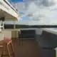 3 days shared trip. View of a serene boat deck with comfortable seating, a small table, and a scenic landscape under a partly cloudy sky.