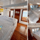 3 days shared trip. Brightly lit cabin with two beds, colorful artwork on the wall, wooden accents, and large windows showcasing natural light.