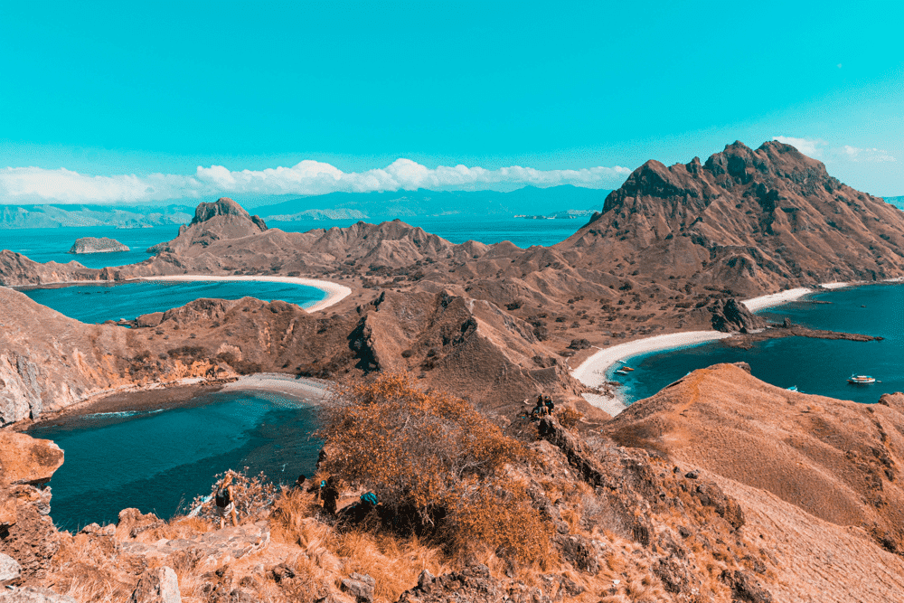 Padar Island Indonesia – A picturesque landscape of rocky hills and turquoise waters, showcasing winding beaches and distant mountains under a clear sky.