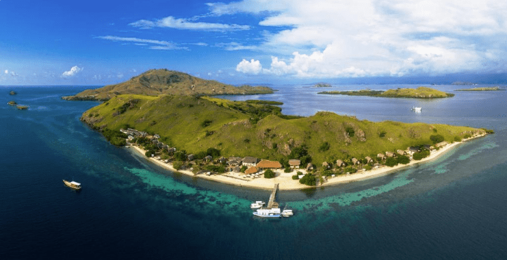 Sebayur Island. Aerial view of a lush green island surrounded by crystal-clear waters and boats docked at a sandy beach.