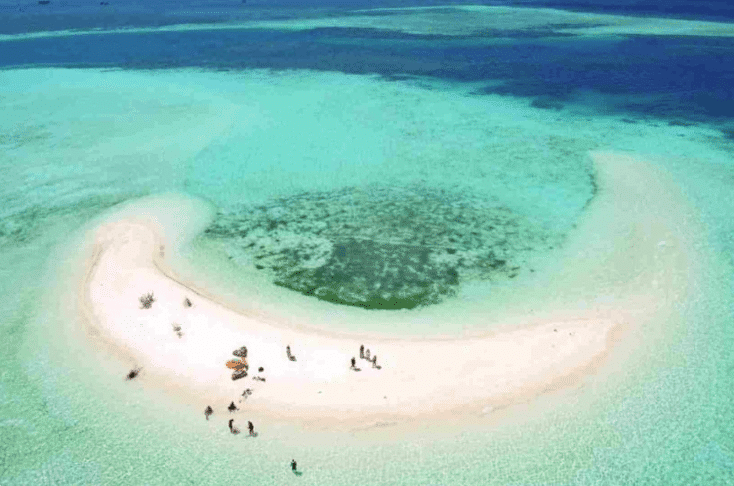 Takak Makassar - Aerial view of a sandy beach on a small island surrounded by turquoise water and people enjoying the serene environment.