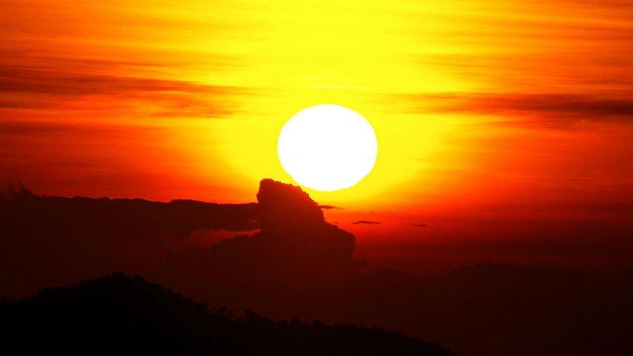 Kelimutu Volcano​ Indonesia. A vibrant sunset casts a glowing orange and yellow hue, silhouetting mountains against the colorful sky.