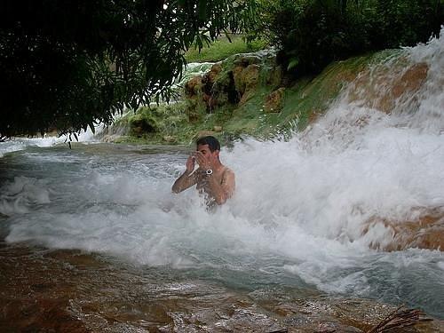 Ngada village. A man sits in a rocky river surrounded by cascading water, enjoying the natural scenery and splashes around him.