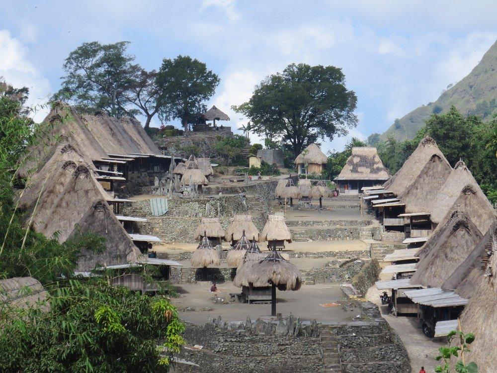 Ngada village. Traditional village with thatched-roof huts, surrounded by lush greenery and mountains under a bright sky.